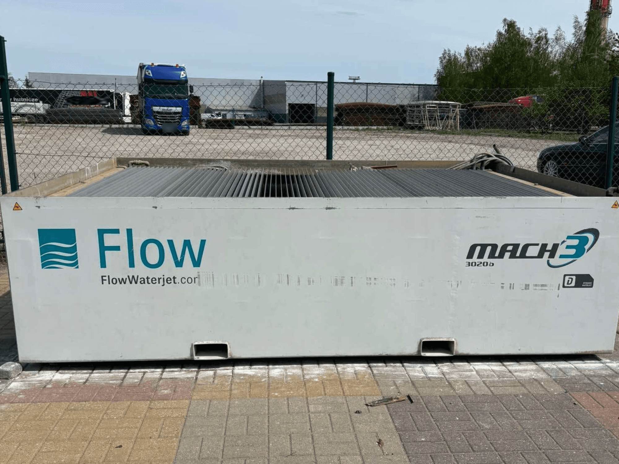 Flow Mach3 3020b waterjet machine shown from the side, featuring a white metal body with a corrugated top and logo.