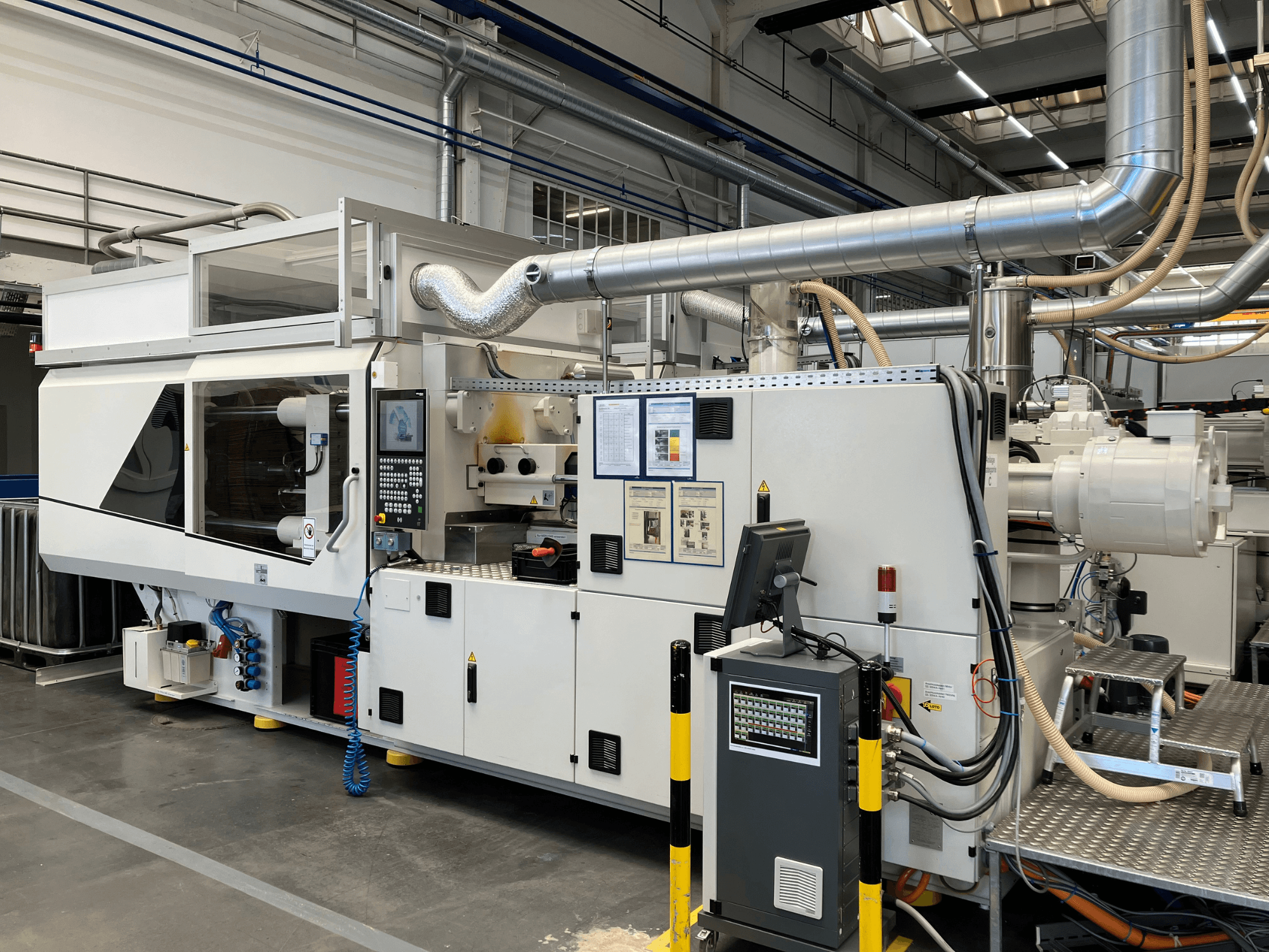 Vorderansicht einer Industriemaschine mit Bedienfeld, Rohren und Bildschirmen in schlichtem weißem Design und technischen Details.