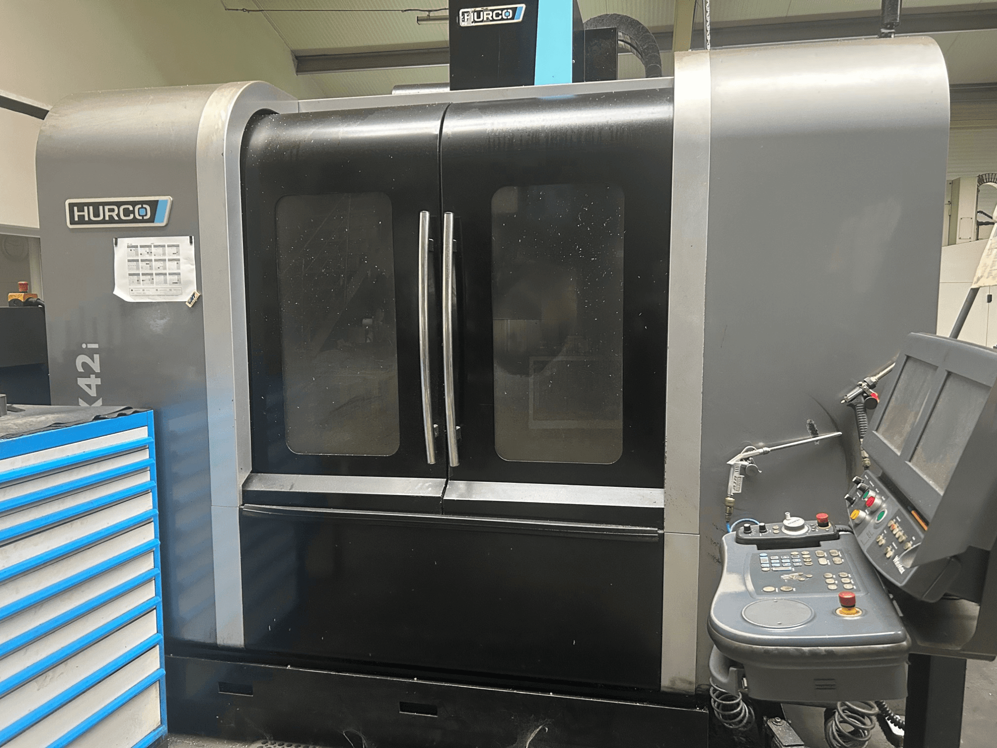 Hurco VMX42i CNC-Maschine, Vorderansicht mit seitlichem Bedienfeld, mit Flügeltüren und sichtbaren technischen Details.