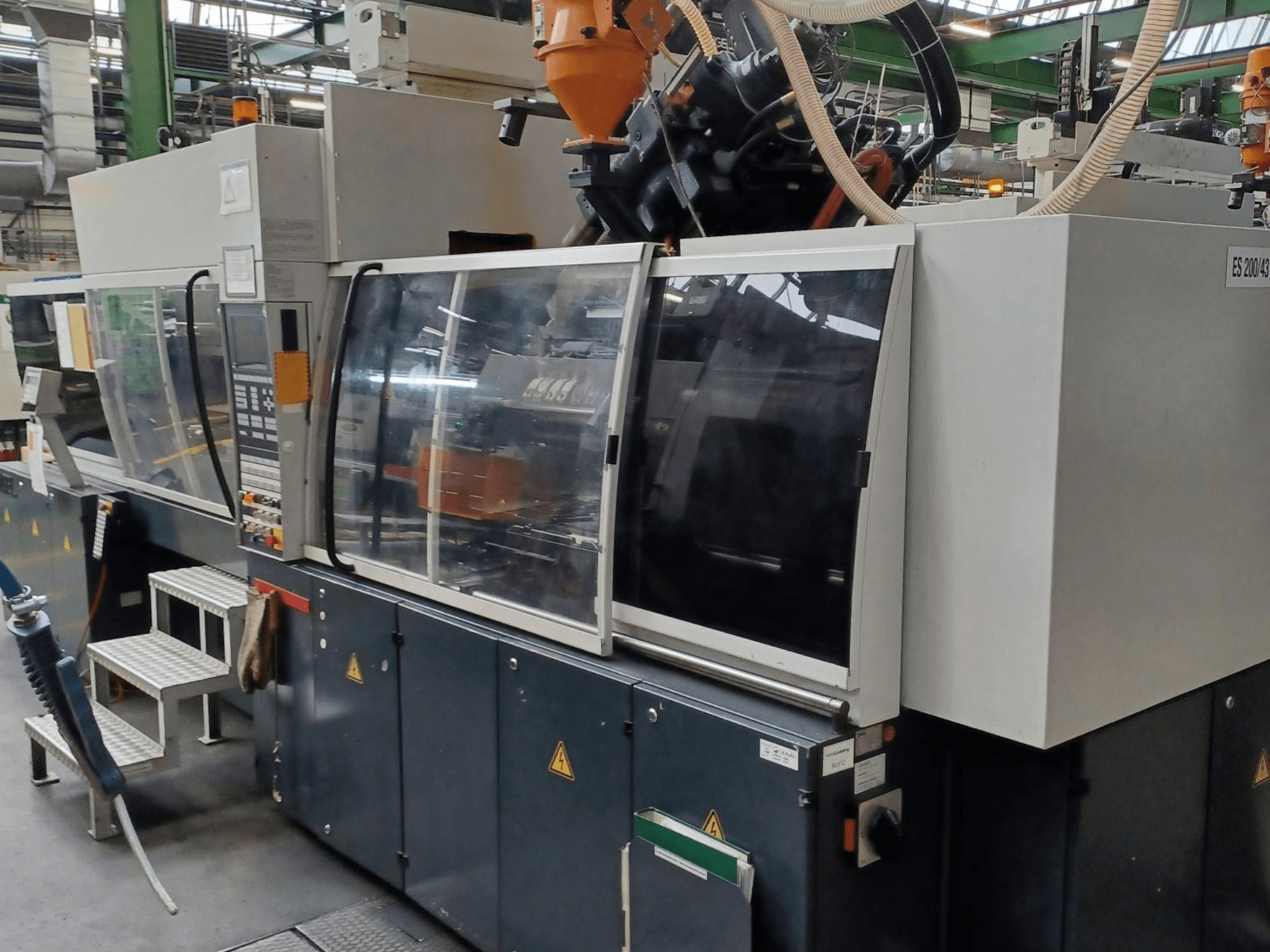 Vorderansicht einer Kunststoffspritzgießmaschine, Marke und Modell unbekannt, mit transparenten Schutztüren und Bedienfeld.