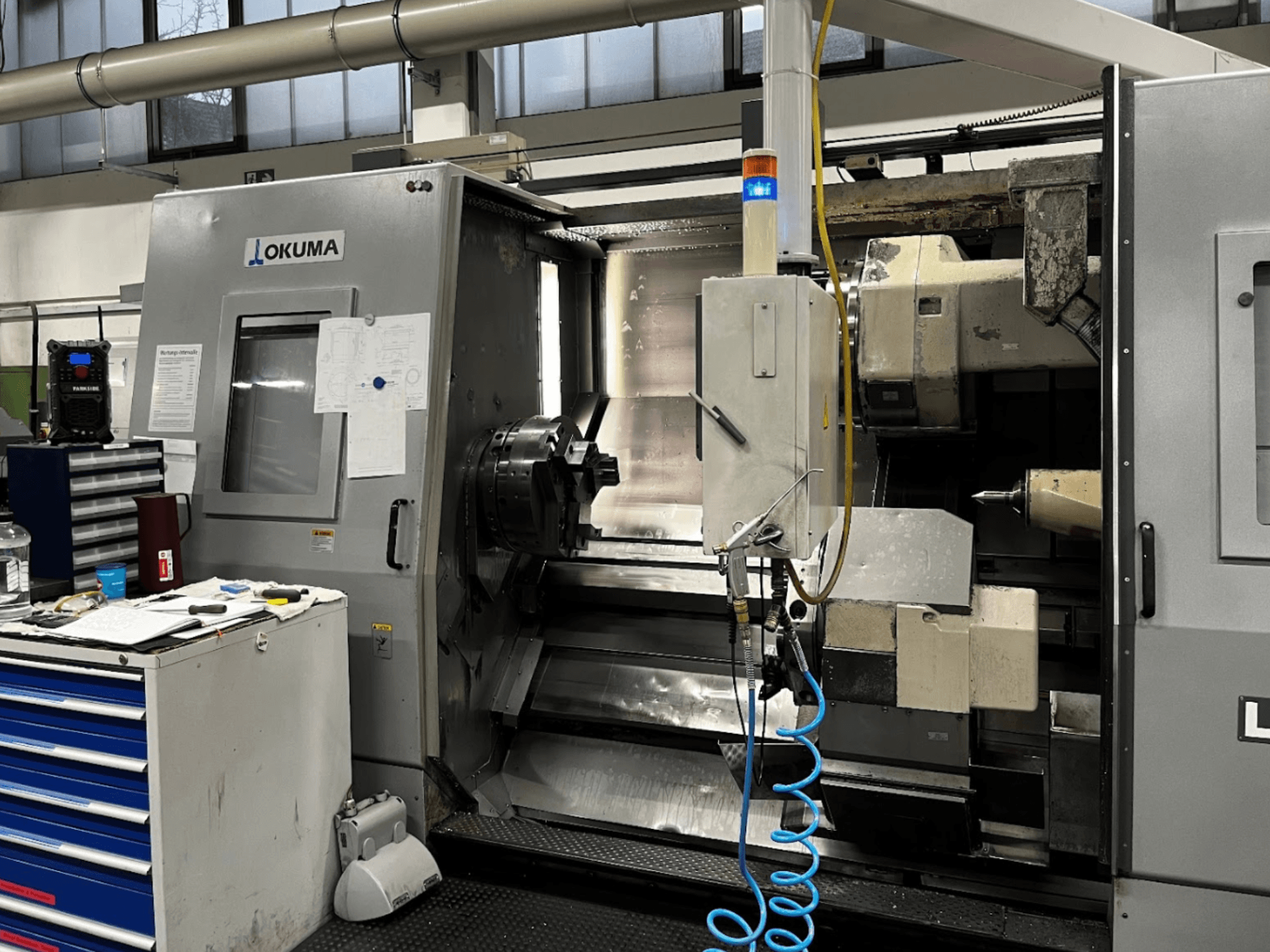 Okuma LU35-M Horizontal-Drehmaschine, Vorderansicht. Mit Bedienfeld, Werkzeugen und großem Spannfutter für die Bearbeitung.