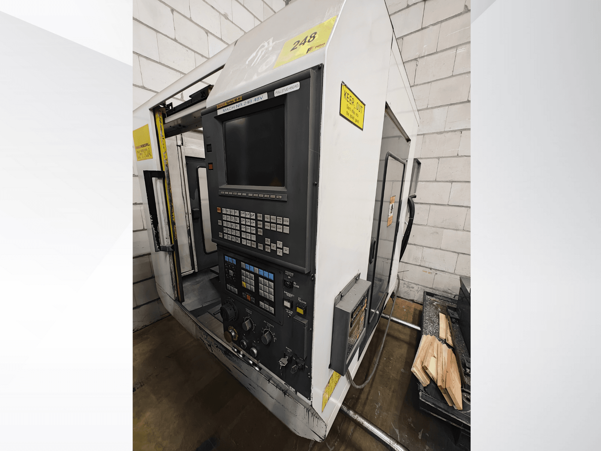 CNC-Maschine Modell Nr. 248, Vorderansicht, mit einem Bedienfeld mit Tasten und Display, daneben Holzteile auf einem Regal.